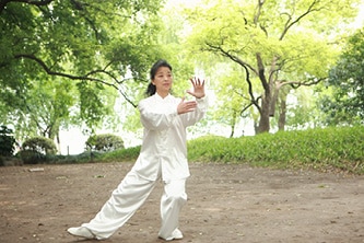 woman practicing tai chi outside in park learn taoist yoga