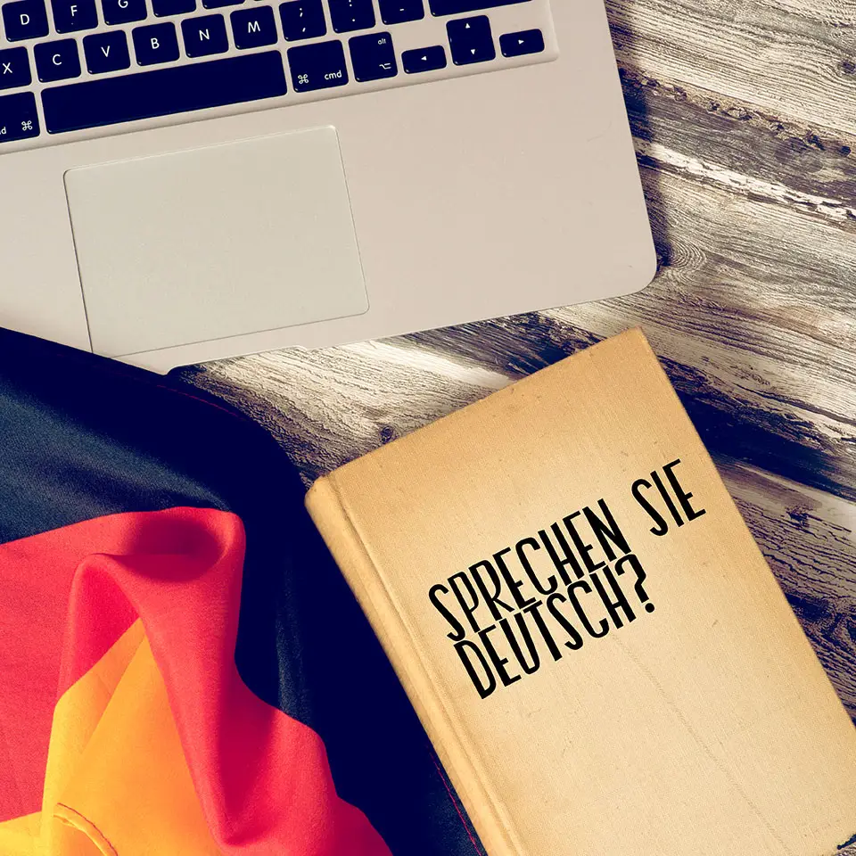 Flag of Germany, a book with the title, "Sprechen sie Deutsch", and a laptop on a tabletop